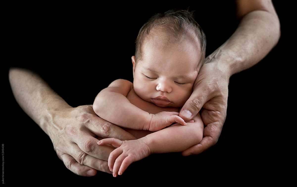Asian newborn in father\'s\' hands in black background