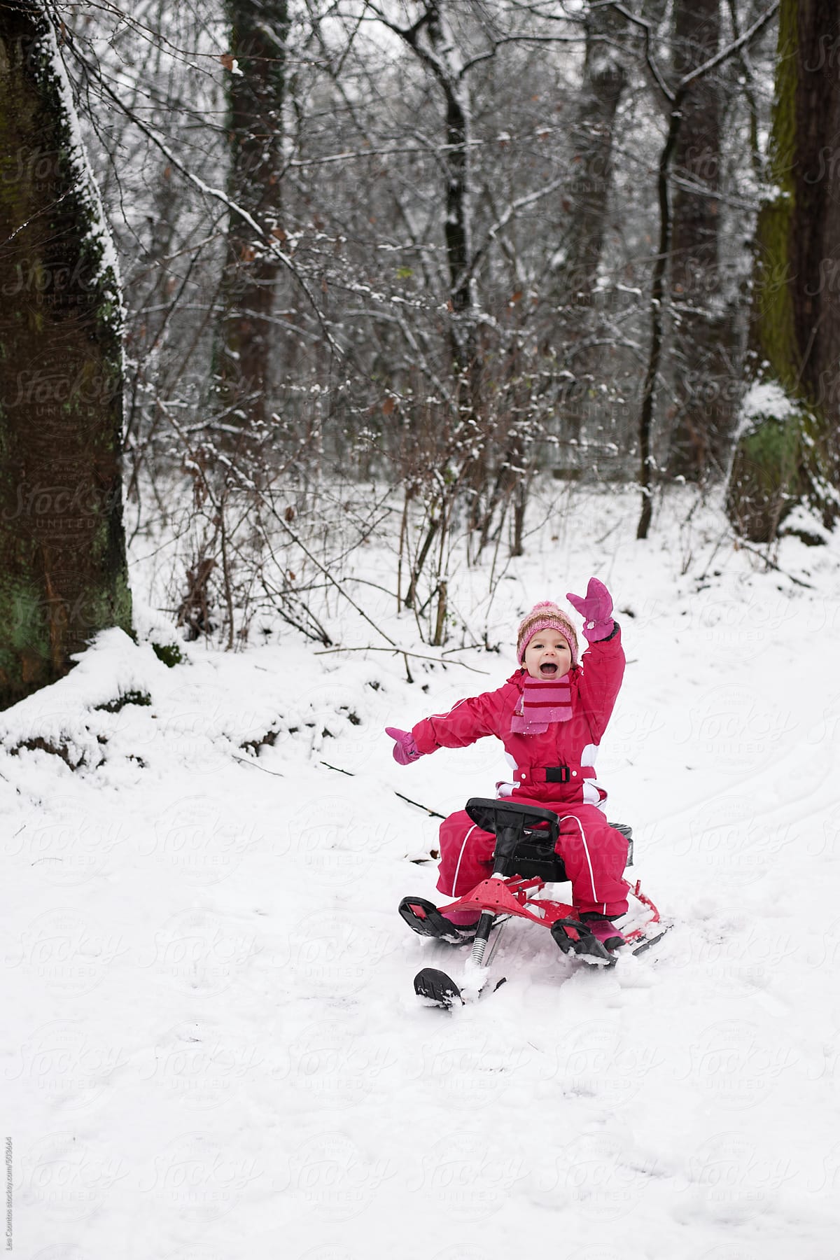 Little girl having fun on a sledge saying hello.