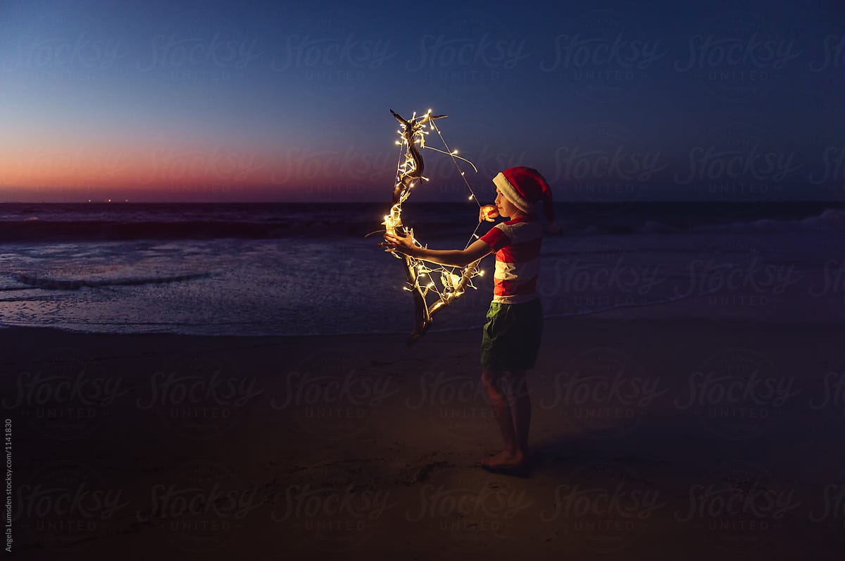 Boy with christmas lights at the beach after sunset