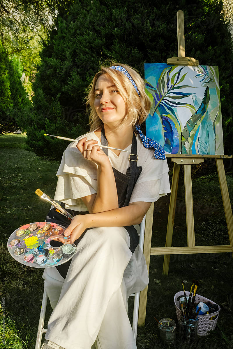 Blonde happy artist woman paints palms in nature