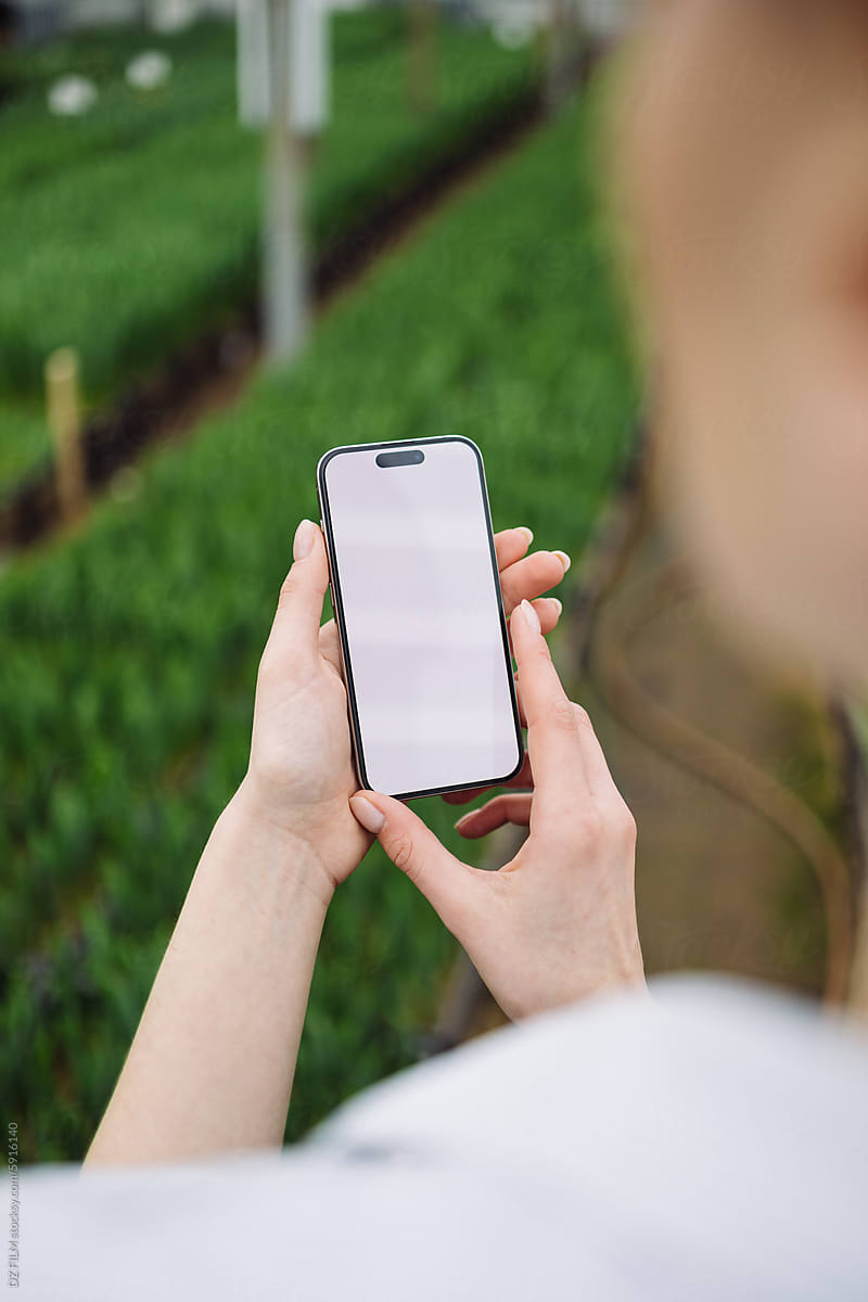 A woman uses a white-screen phone in a greenhouse