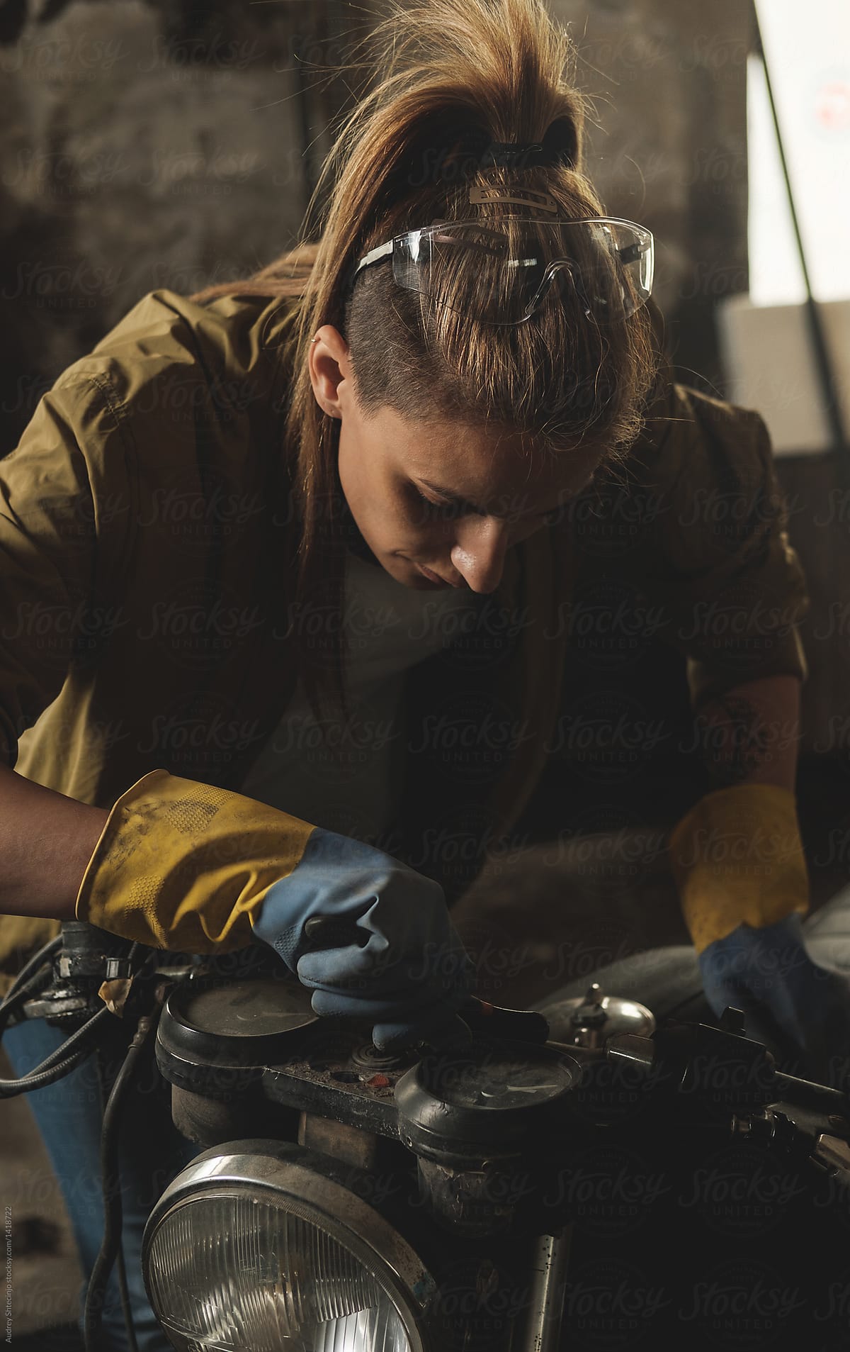Young female working on restoration of old /vintage motorbikes in old rusty motorbike garage/workshop