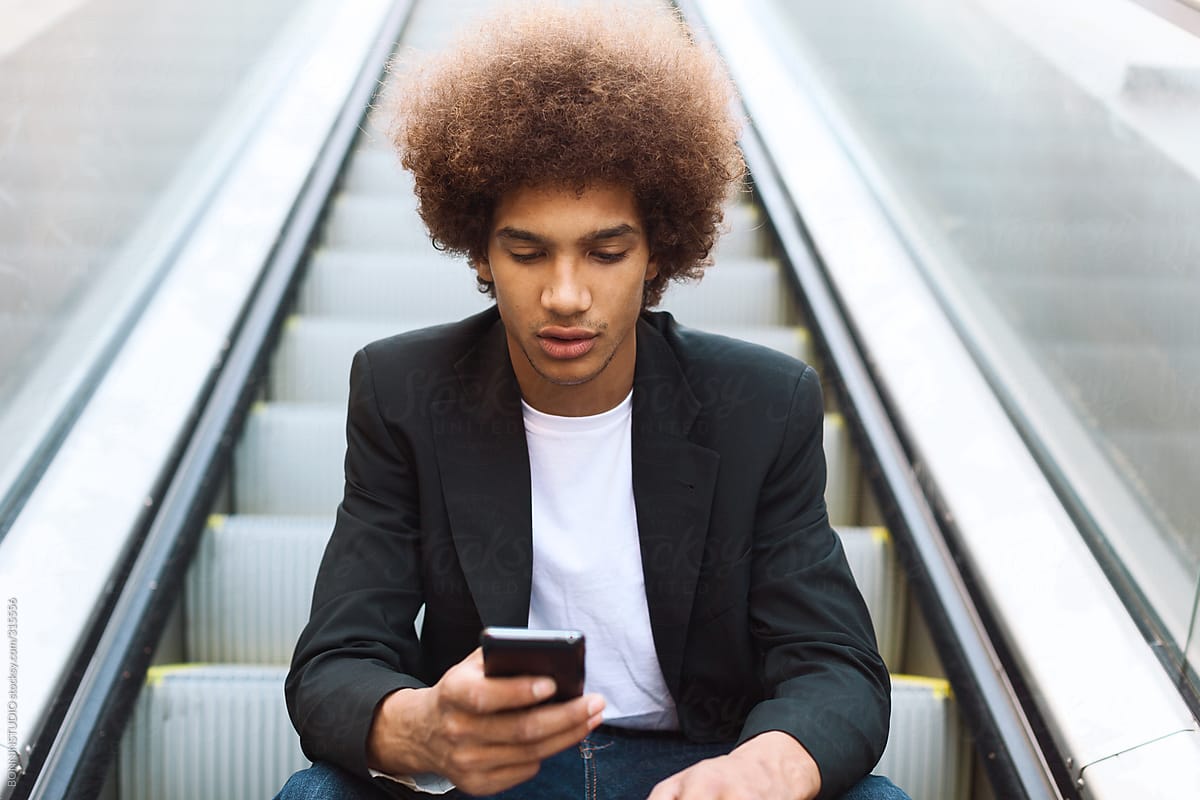 Young afro american businessman sending text message on his mobile phone sitting on an escalator.