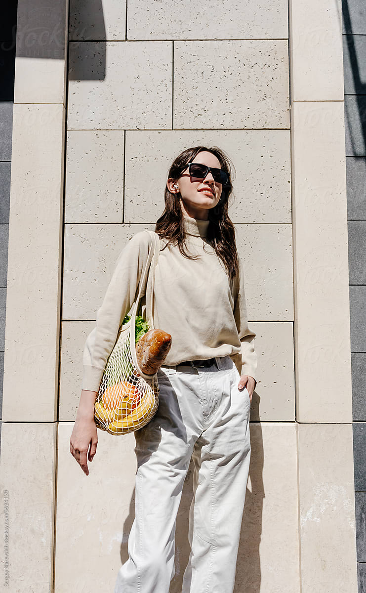 Young trendy woman in sunglasses with groceries in mesh bag