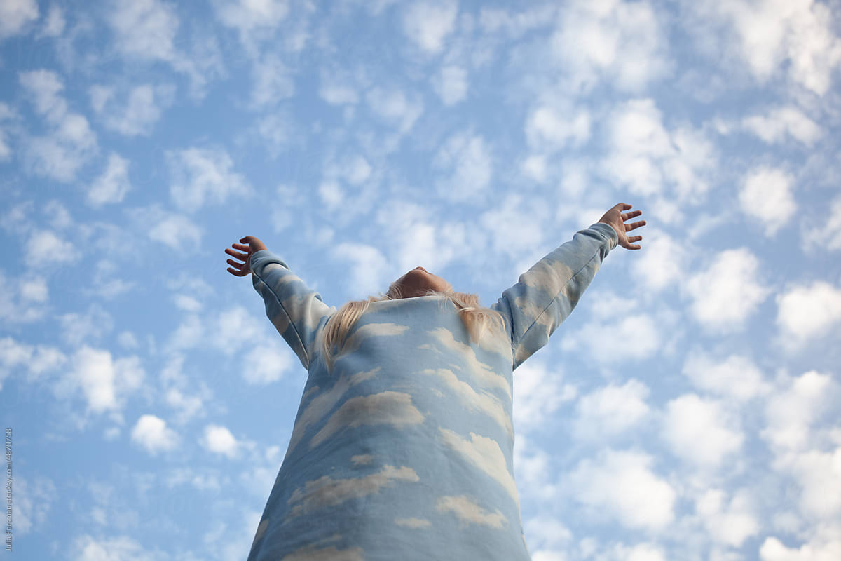 Tween girl reaches into a big blue sky with white clouds. by Julia Forsman for Stocksy United