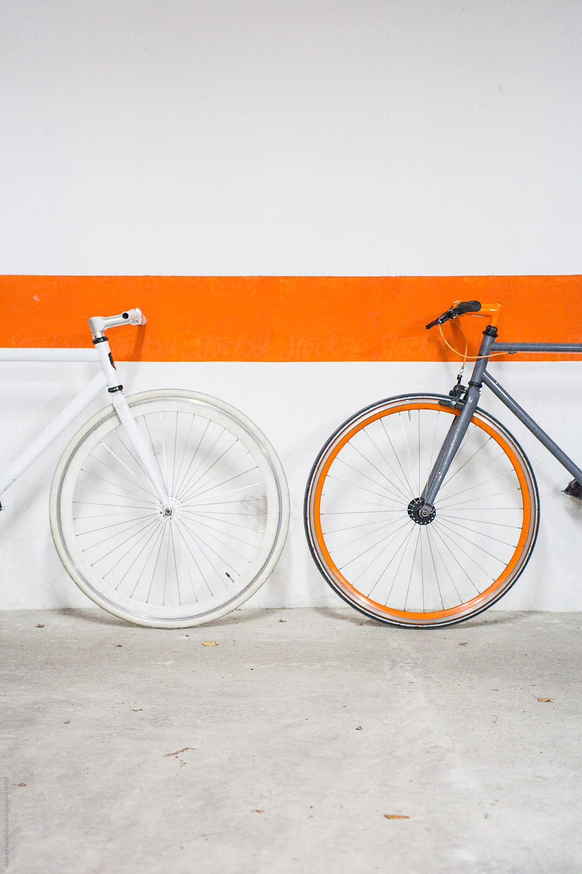 Two fixie bikes with orange line on wall behind.