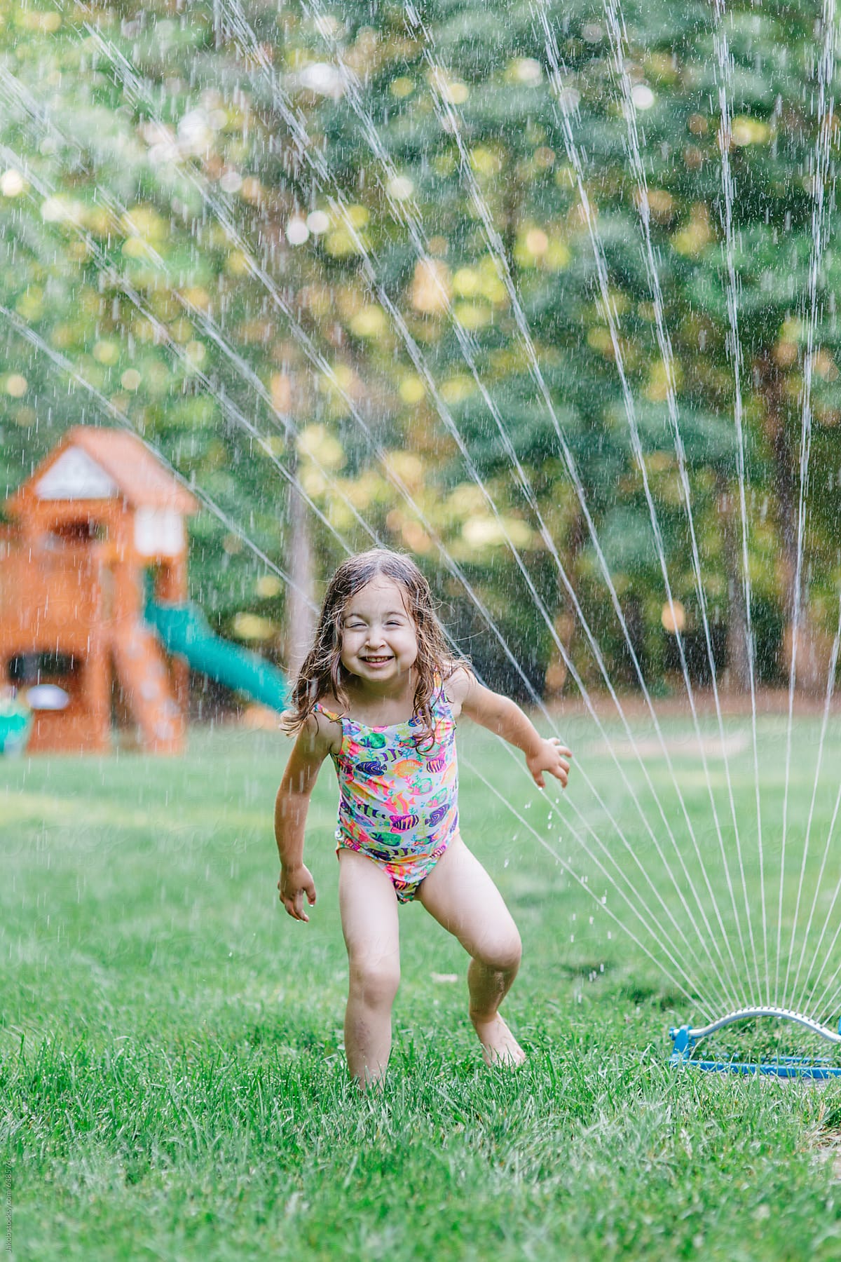 Cute toddler playing with a sprinkler in a yard