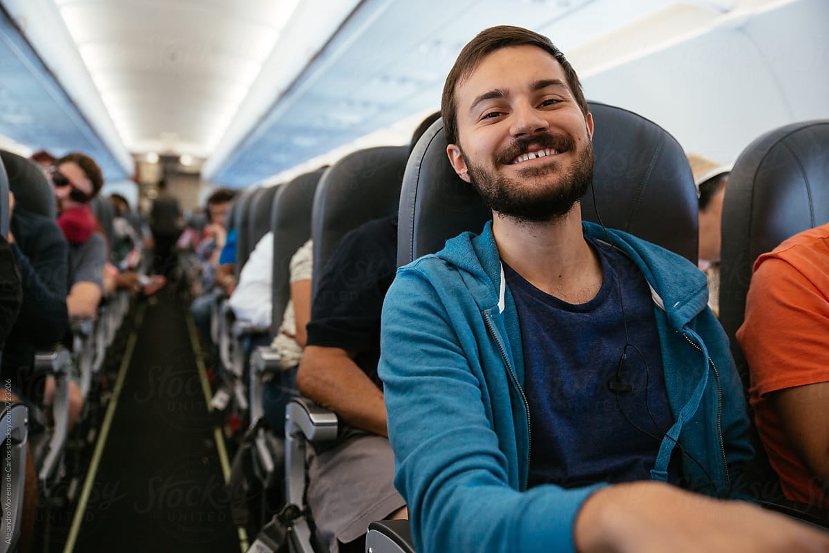 Young smiling man with headphones sitting on an airplane during a flight