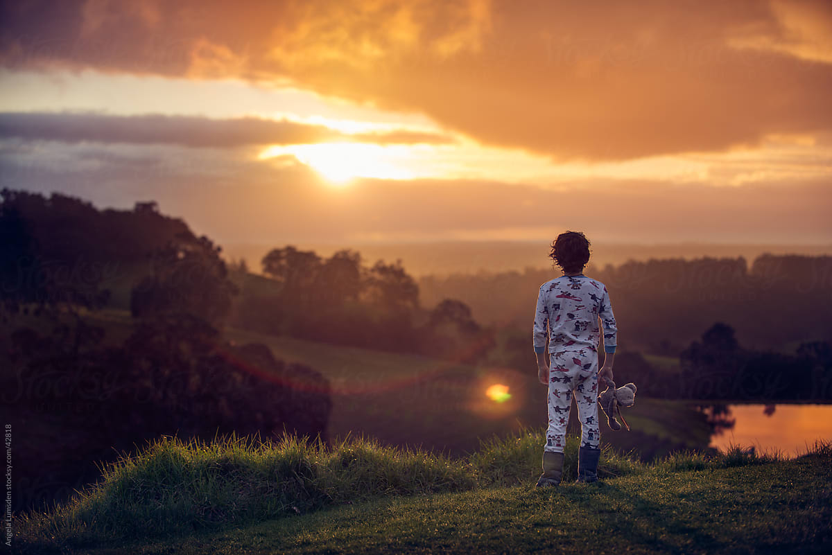 Young boy standing watching the sunset in the country