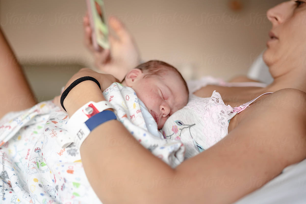 Mother looking at mobile phone in hospital bed