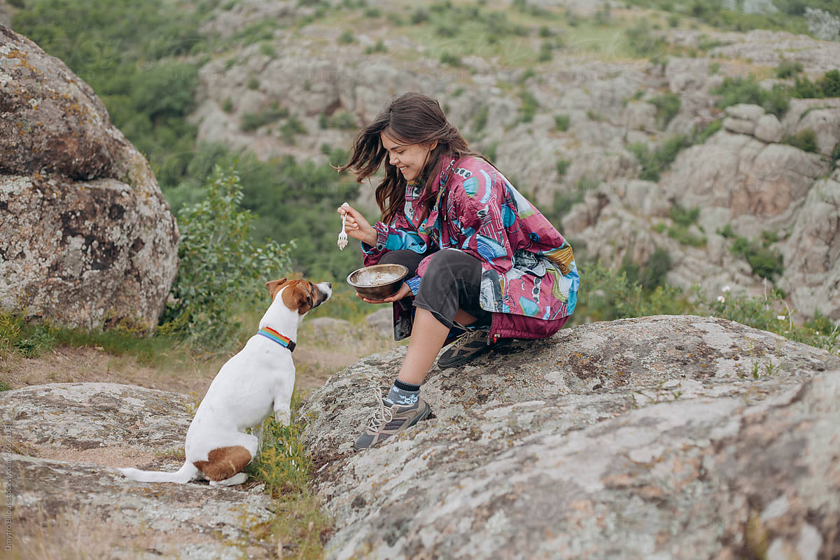 girl traveler sits on a stone and feeds a dog