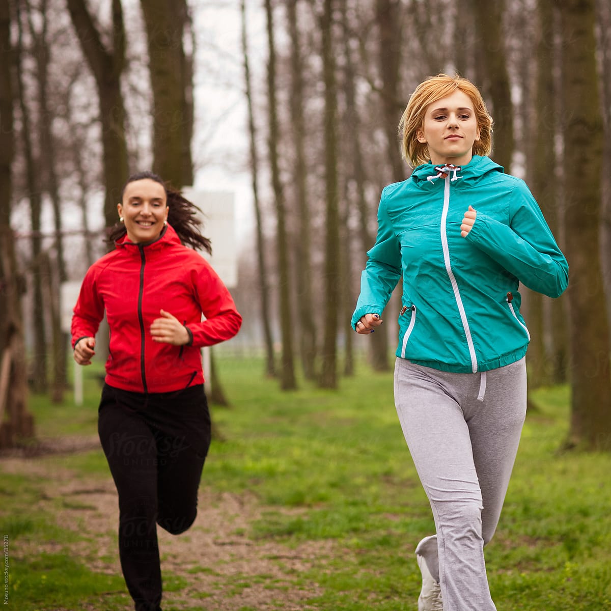 Two women jogging in the park on a rainy spring day.