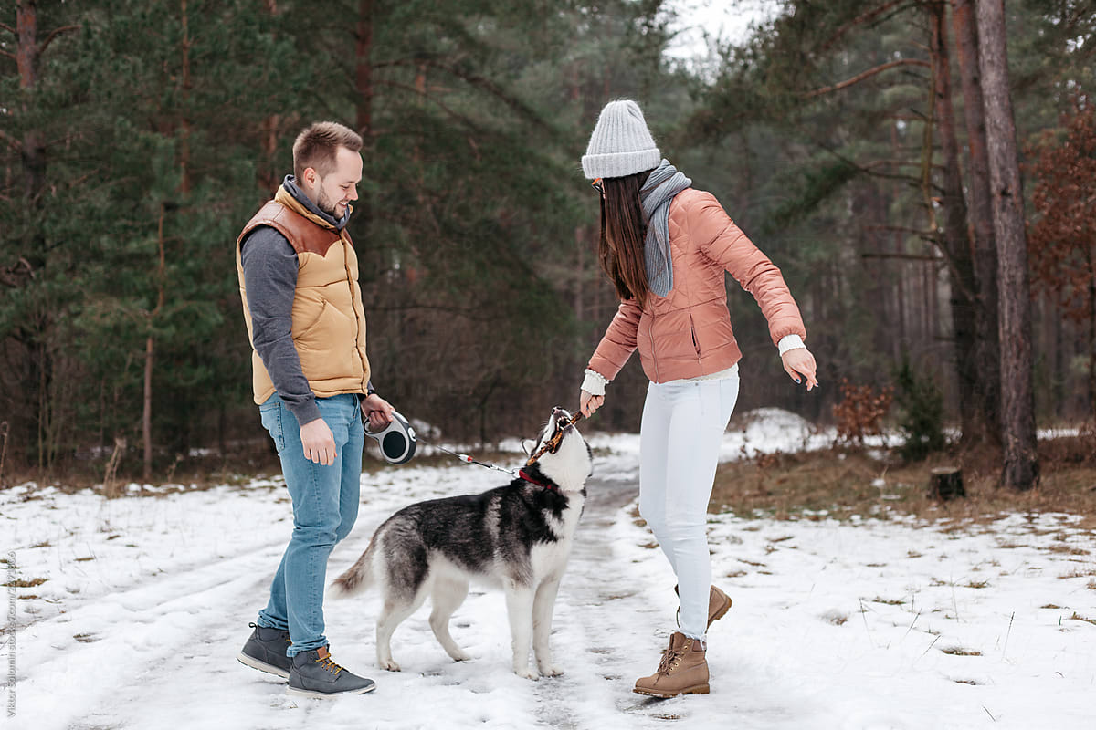 Young active beautiful couple have fun outdoor in winter with dog near the river in forest