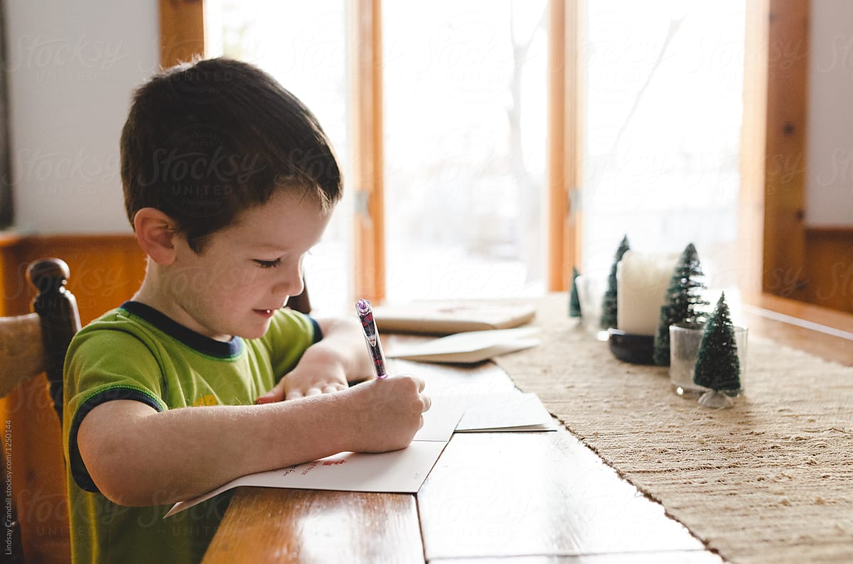 Little boy sitting at the kitchen table signing Christmas cards