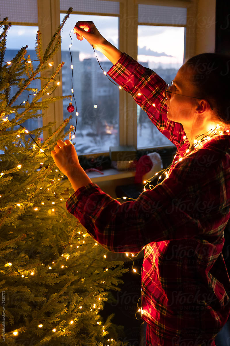 woman in red pajamas decorate Christmas tree with twinkle lights home