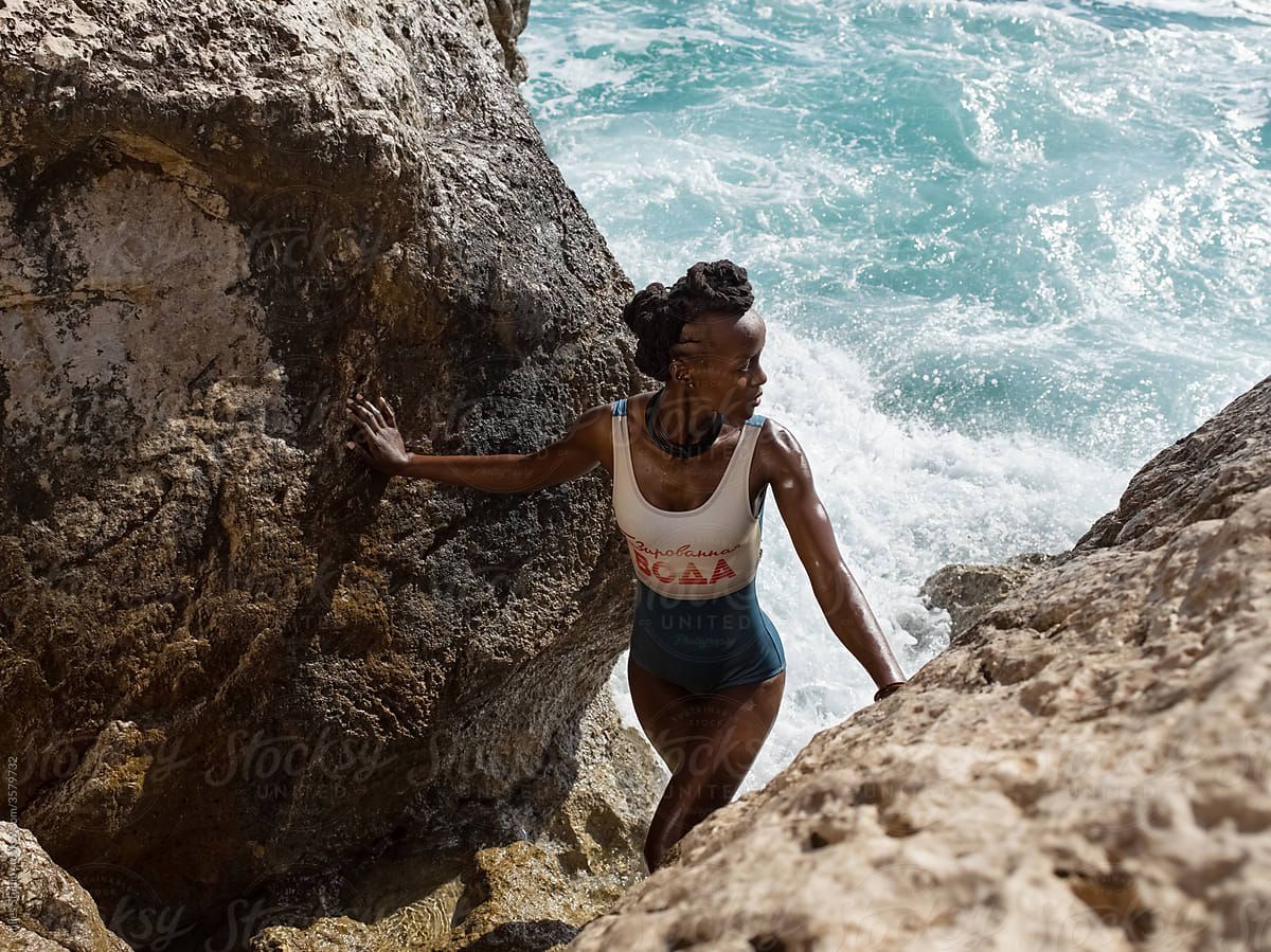 Black woman admiring sea while climbing rock