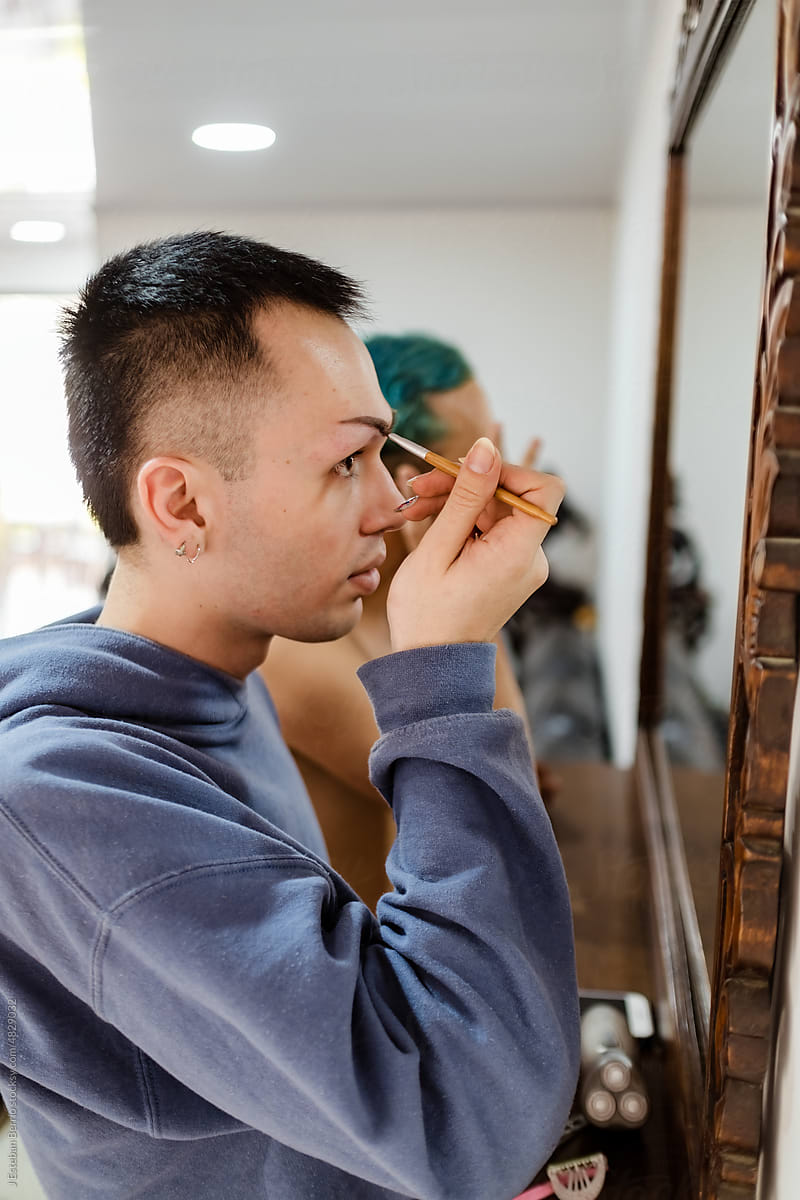 Queer person painting his eyebrows with a brush