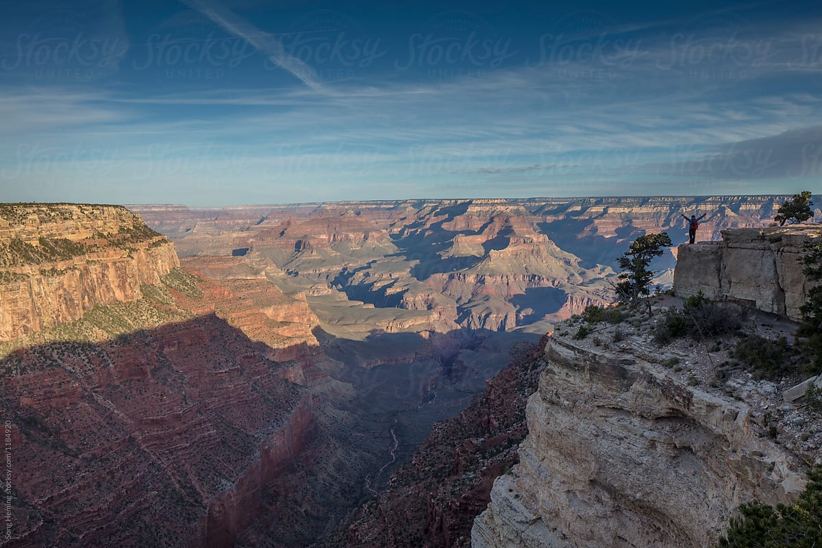 Hiker arms outstretched stand on cliff edge Grand canyon