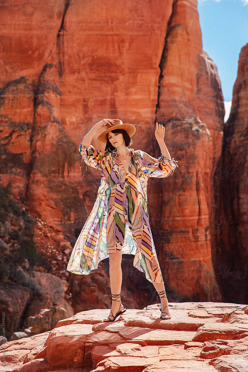 Stylish Cowgirl in dress stands in front of rock formation.