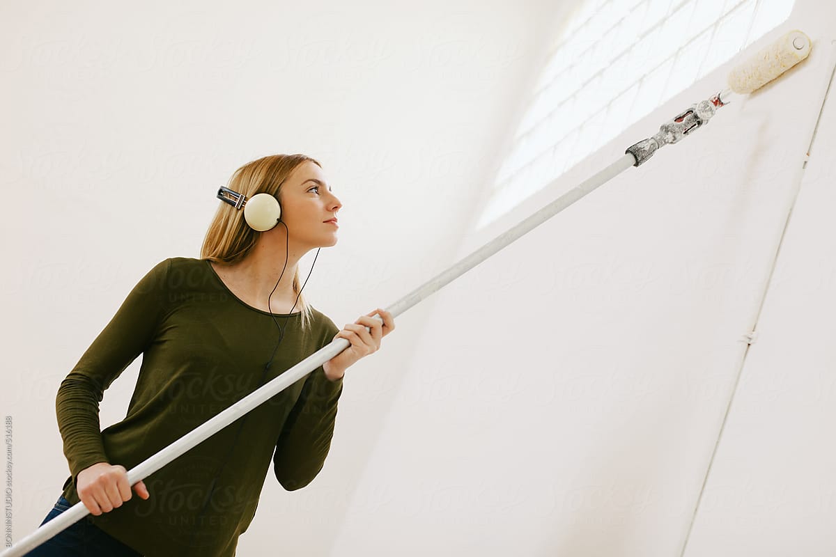 Young woman painting white wall with paint roller on living room.