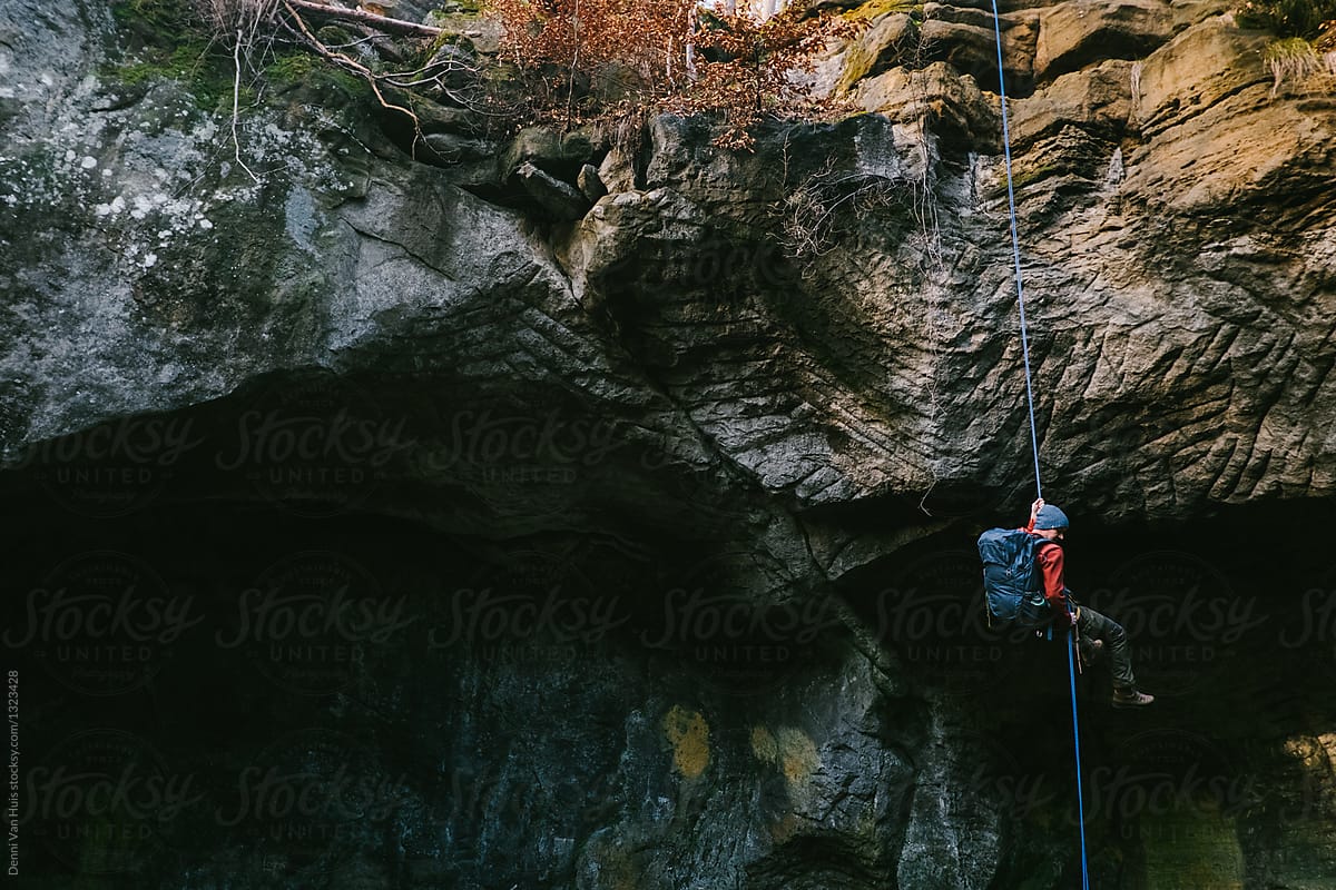 A man climbing down a cliff face, the descent off a cliff.
