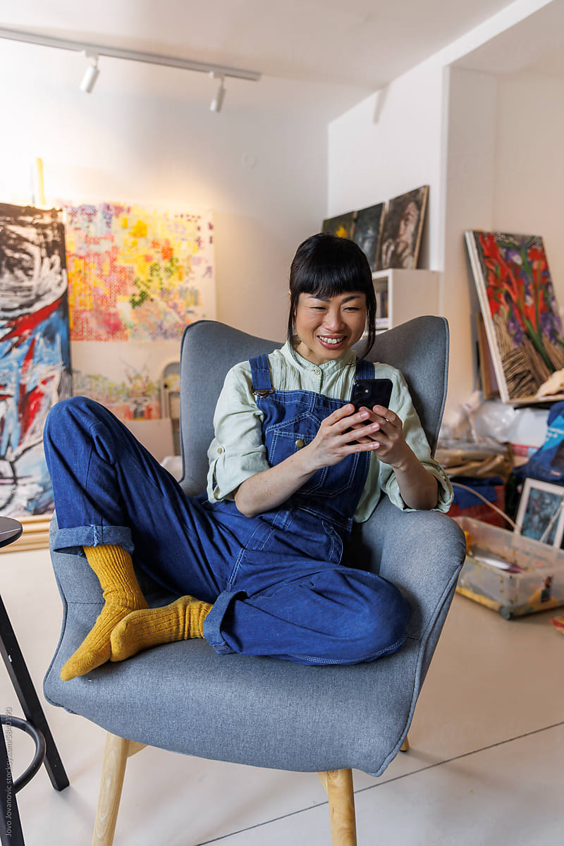 Smiling woman using smart phone on chair at studio