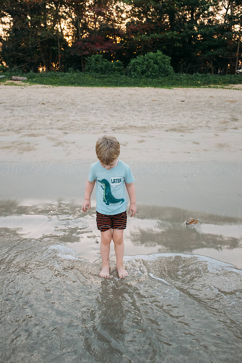 A young child stands in the water at the edge of the sea