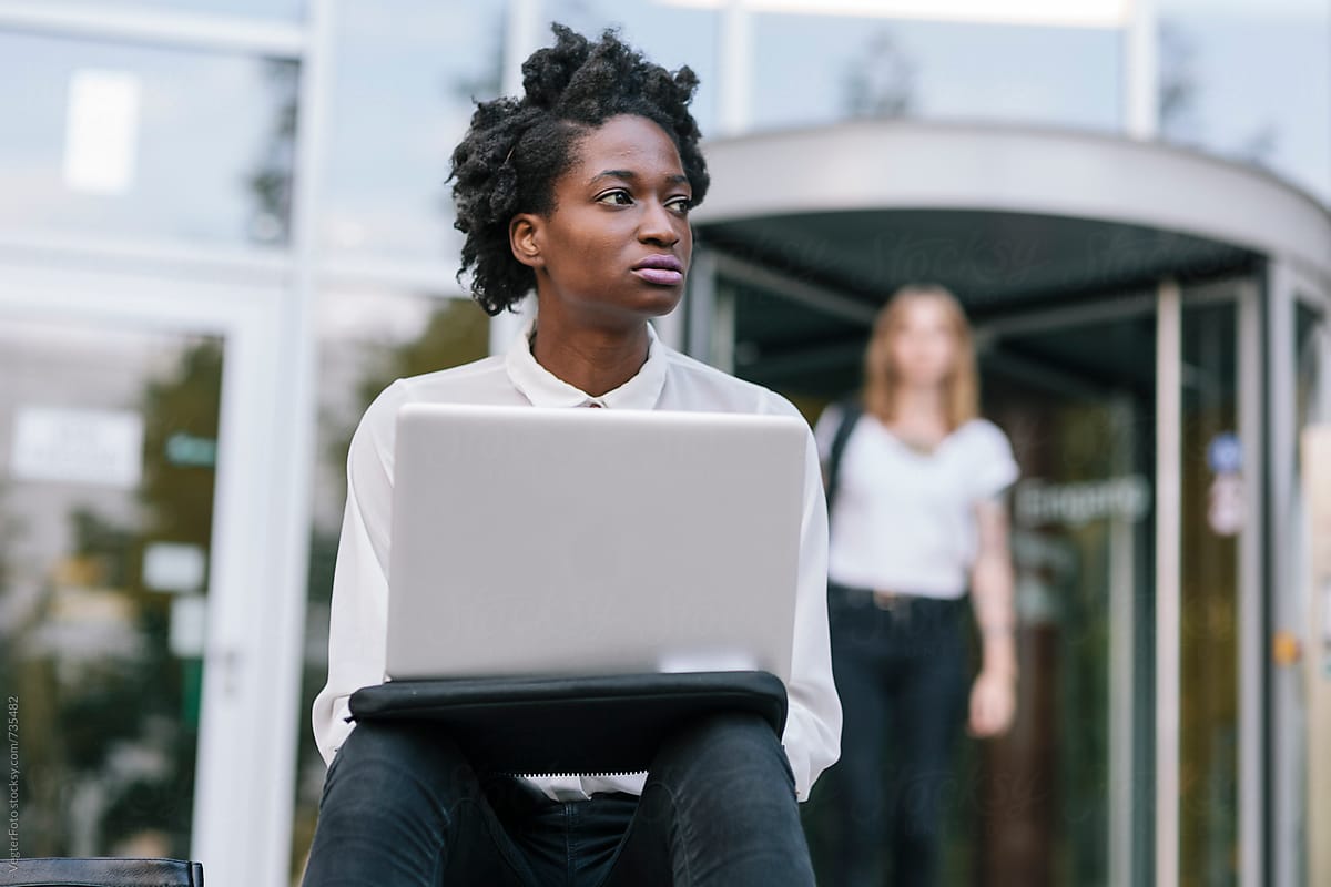 Black woman with Laptop  sitting in front of Building