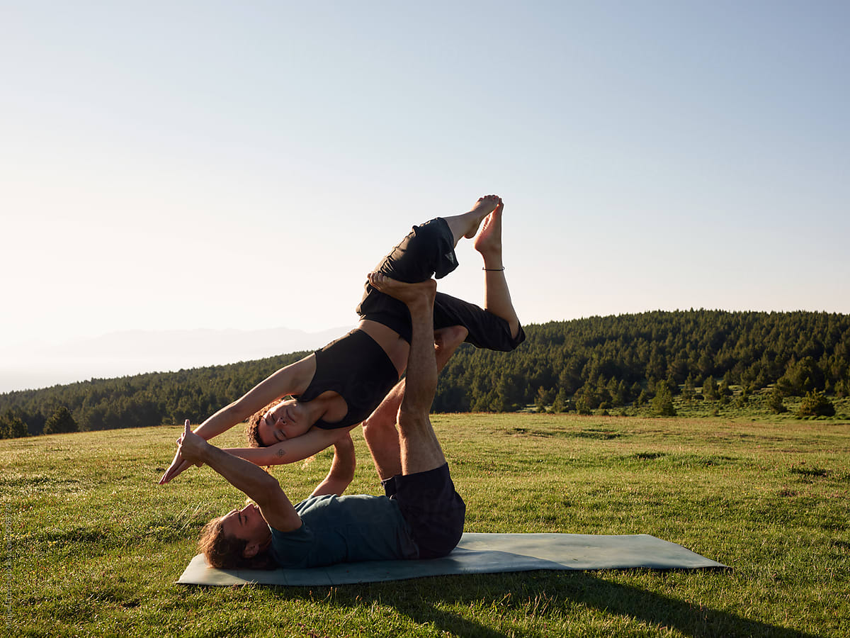 Couple doing balancing pose of acro yoga on sunny meadow
