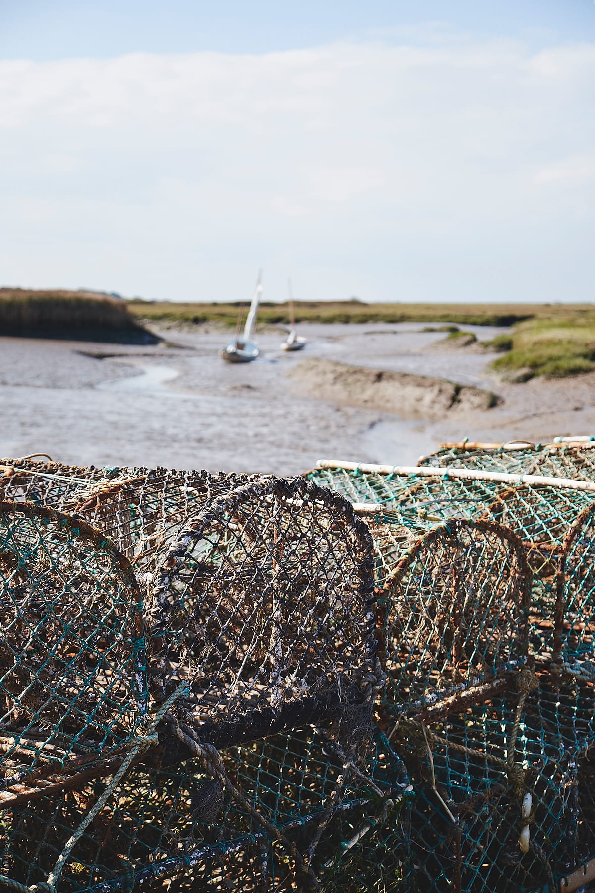 Lobster pots and sailing boats at low tide. Brancaster Staithe, Norfolk, UK.