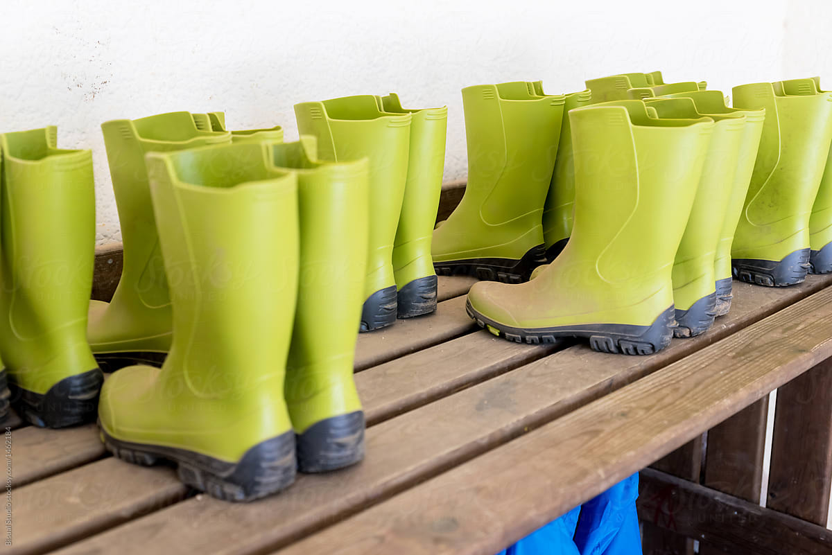 A row of bright green rain boats hang above a bench with matching rain boots below.