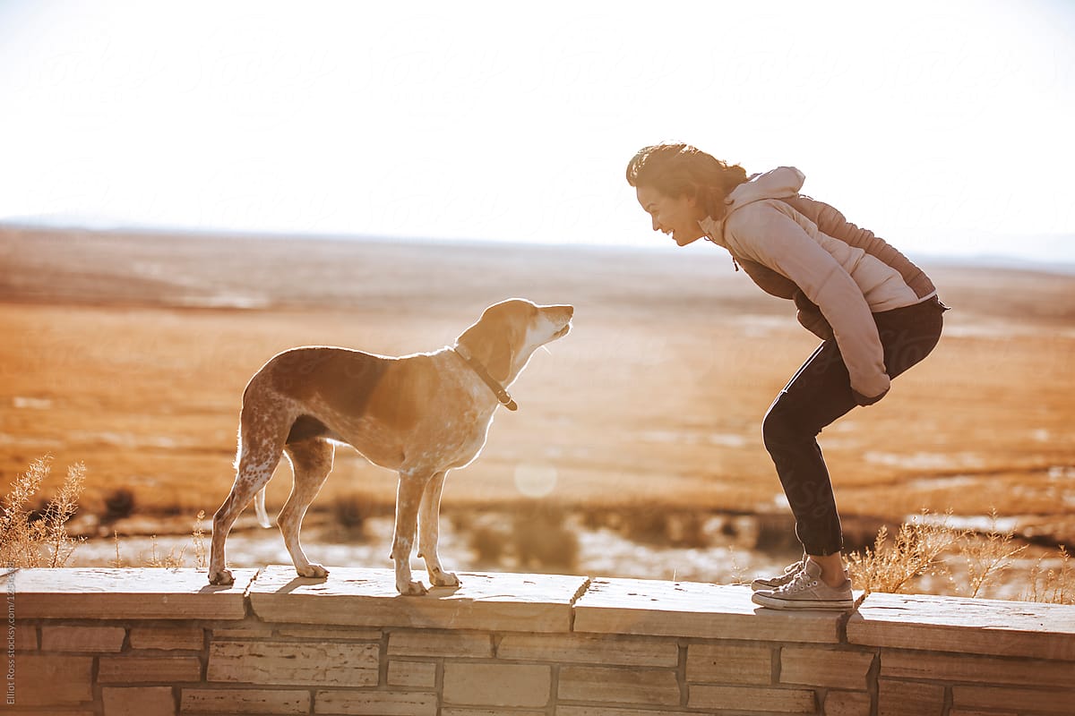 A young woman talks to her dog at sunset