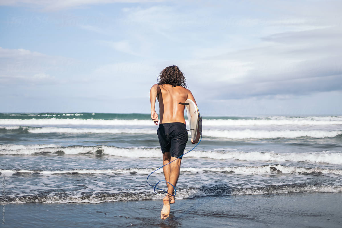 Rear view of a surfer running into the sea