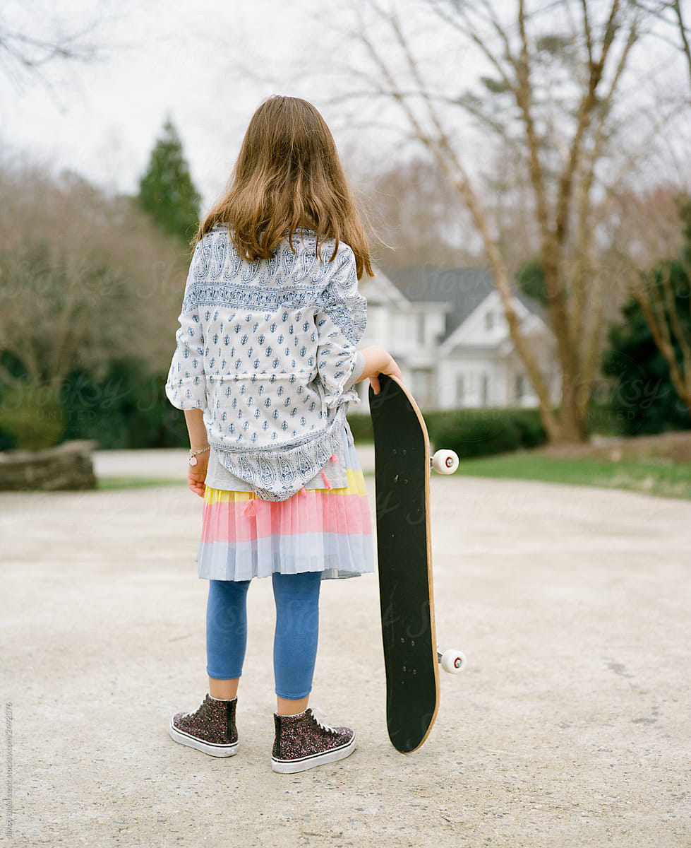 Young girl in a colorful outfit getting ready to ride her skateboard down a driveway