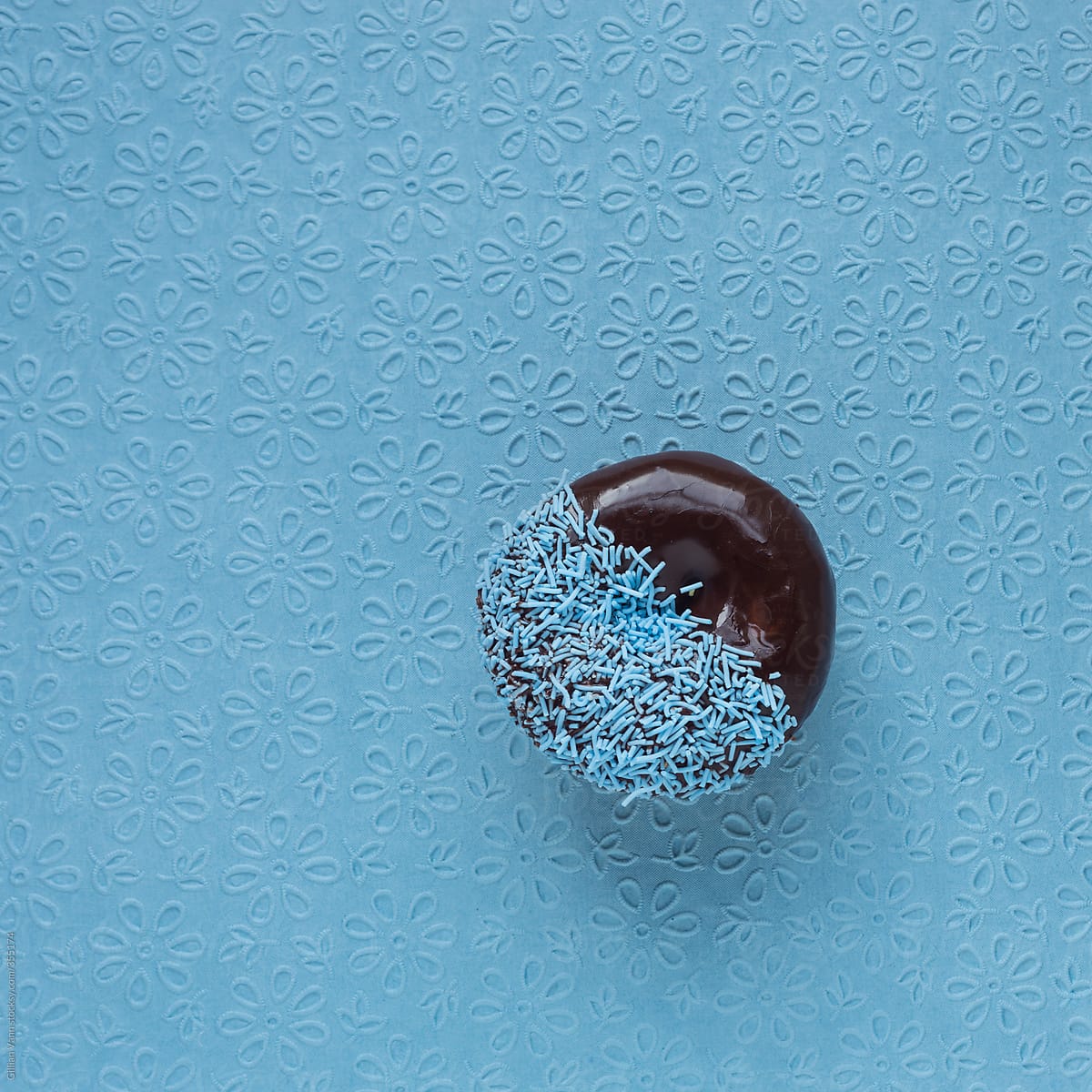 donut with chocolate icing and blue sprinkles on textured blue background