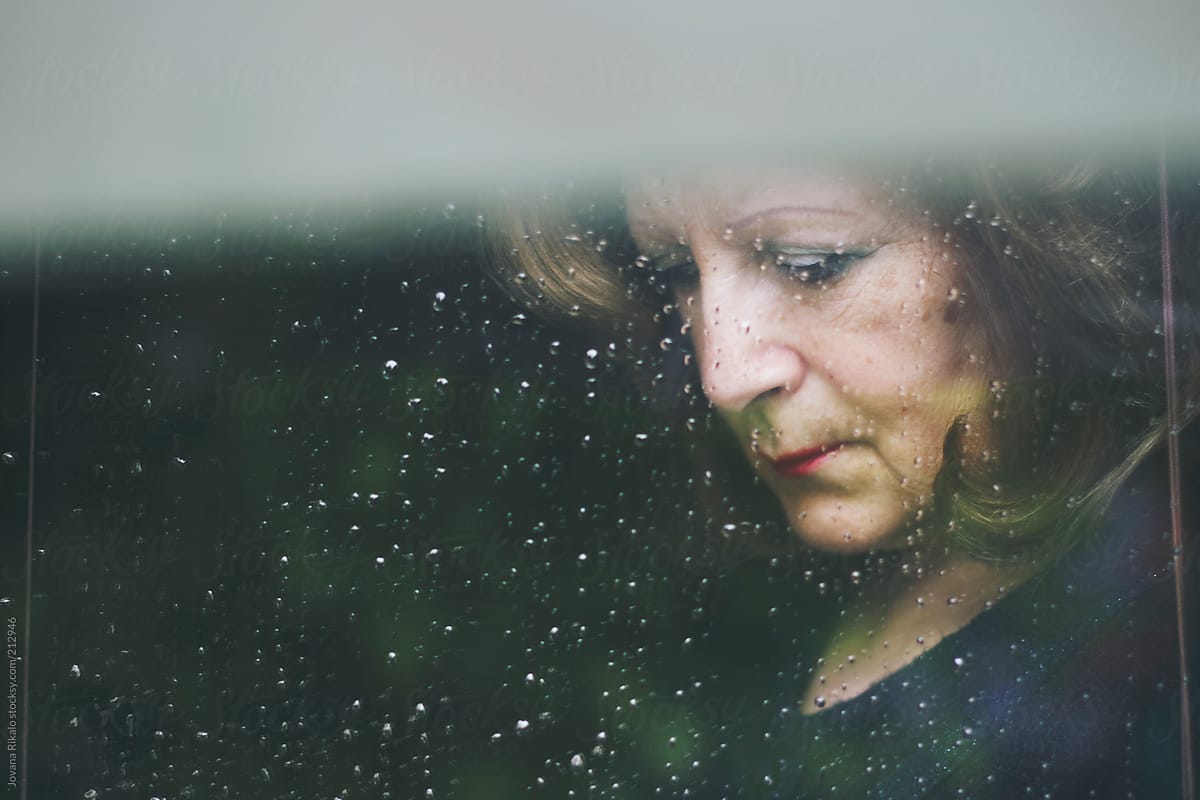 Mature woman standing at the window watching the rain