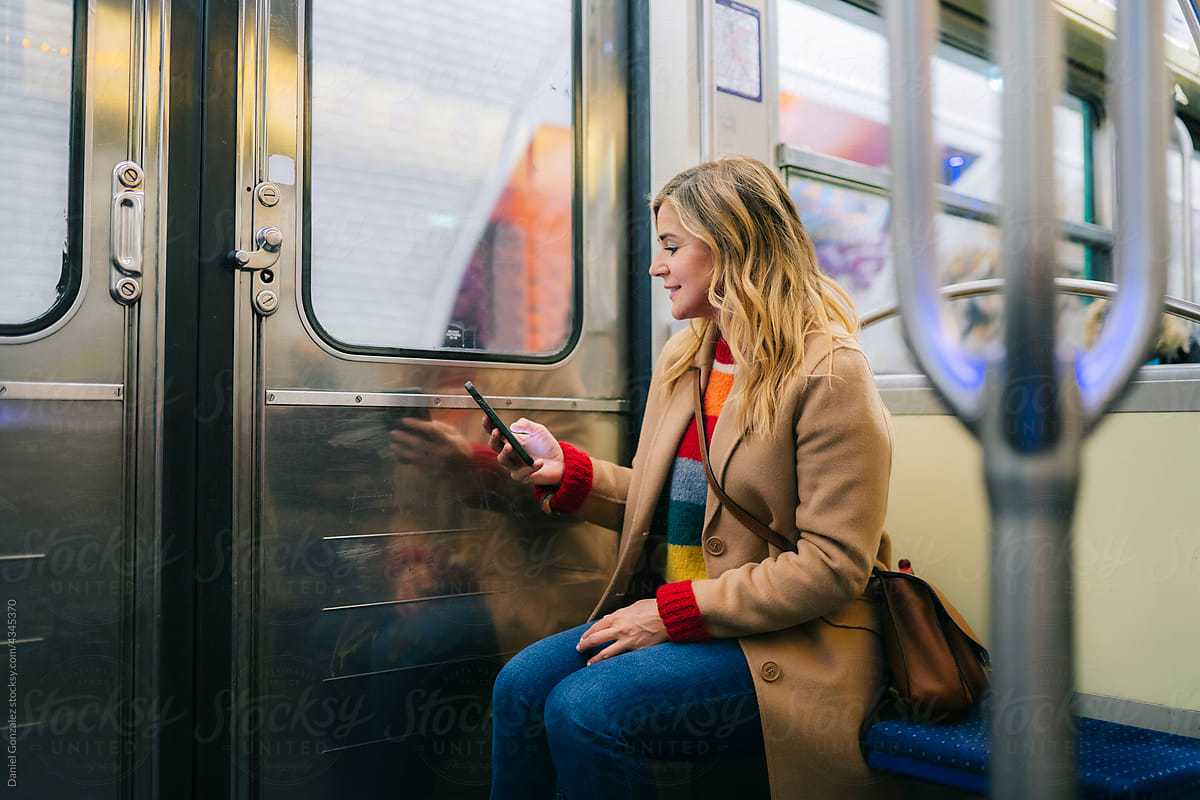 Smiling young lady messaging on smartphone in train