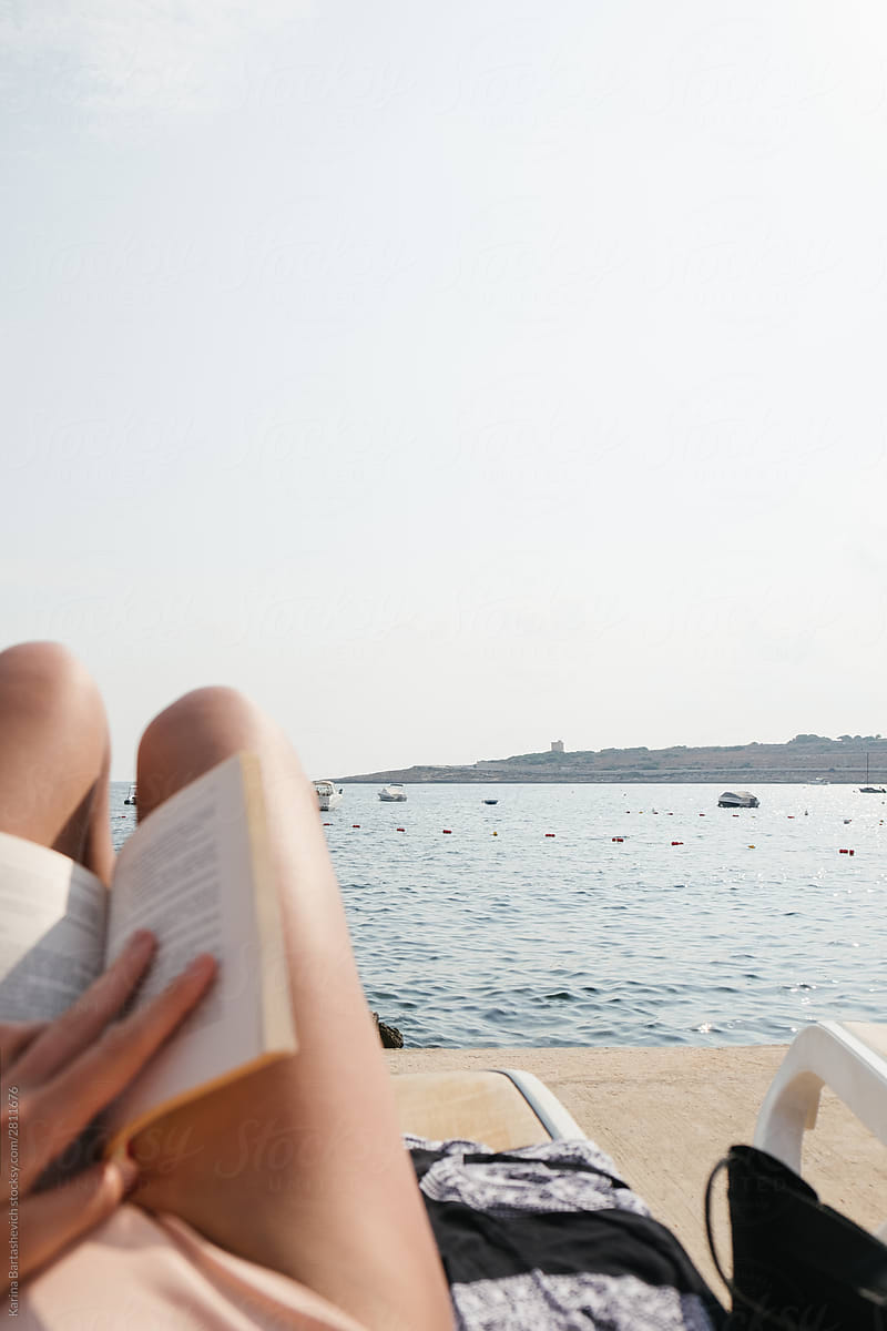 girl in a light bathing suit reads a book by the sea on a yellow deck chair