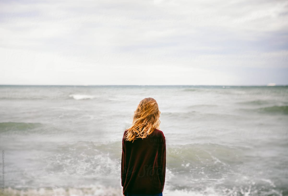 Blonde woman looking at the sea  with the wind  blowing in 