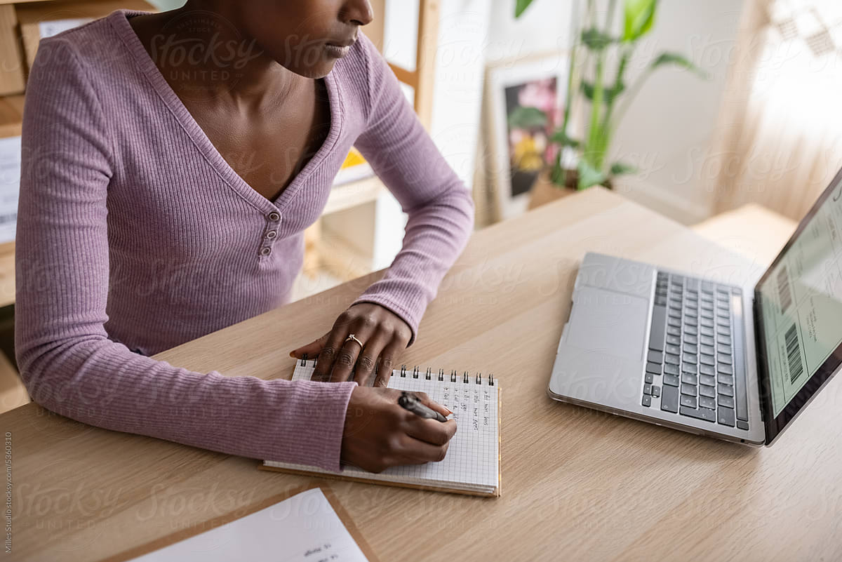 Crop black female employee making list in notepad