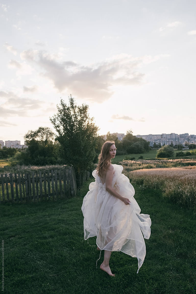 blonde runs along the grass in a white airy flying dress turning to the camera