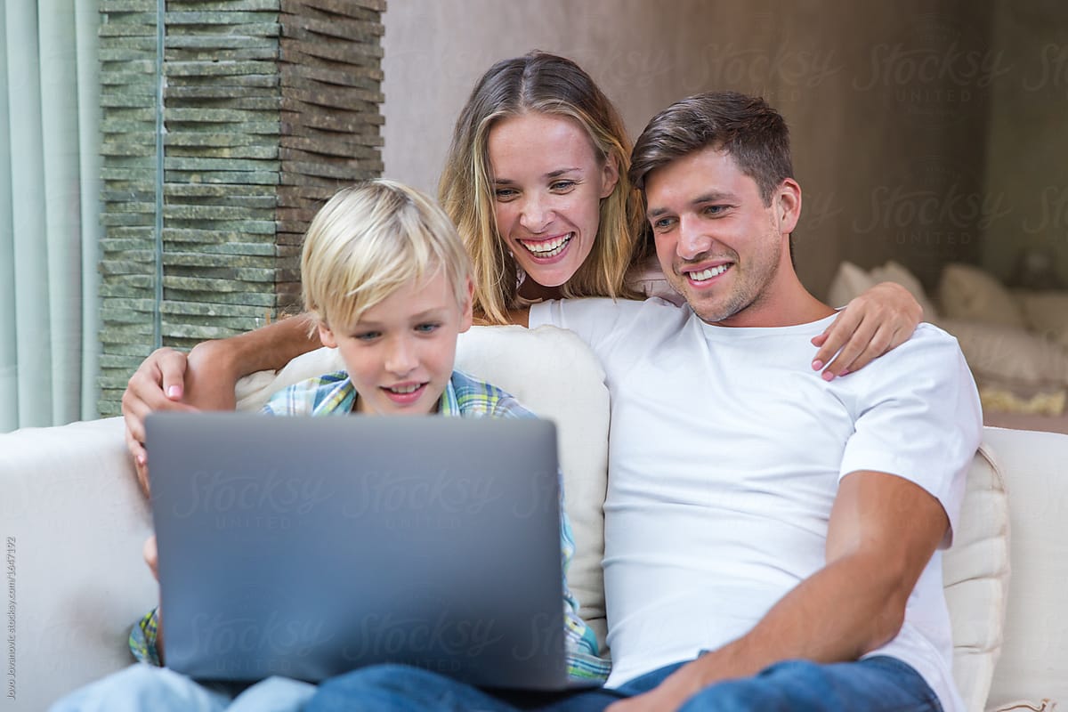 Family Smiling As They Watch A Movie On A Laptop At Home By Jovo