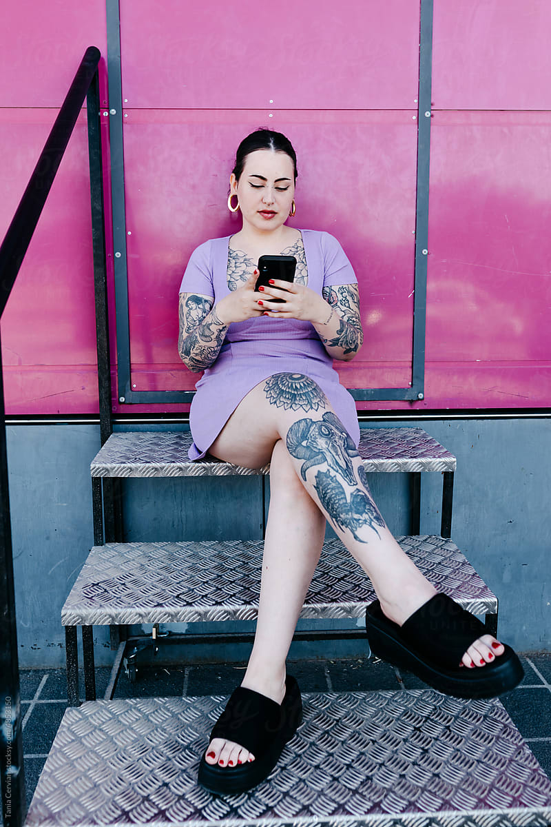 Tattooed brunette using smartphone on steps
