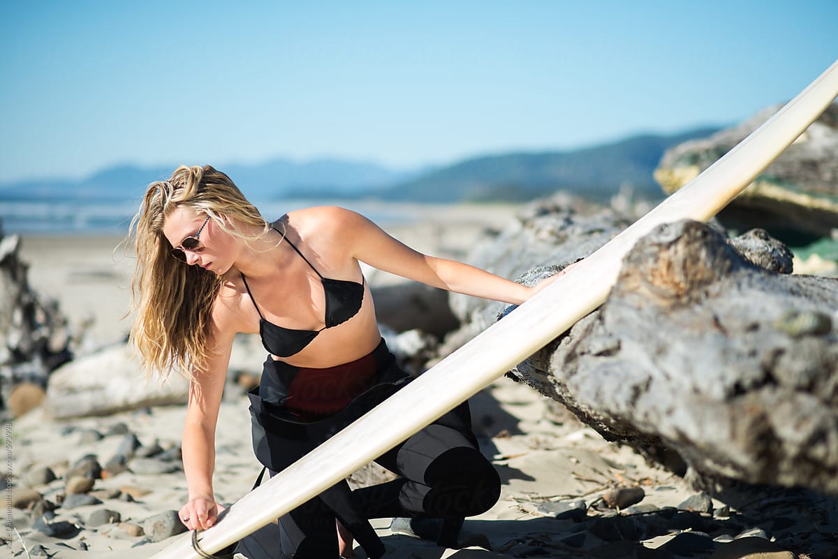 Young beautiful blonde surfer chick waxes her surfboard.
