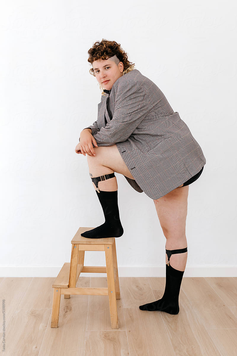 Stylish young queer leaning on knee with foot on stool