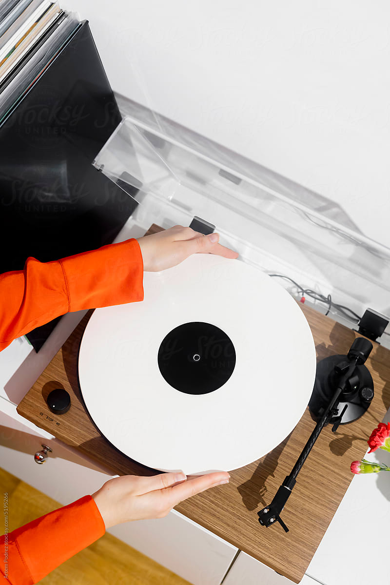 Hands install a vinyl record on a record player to listen to m