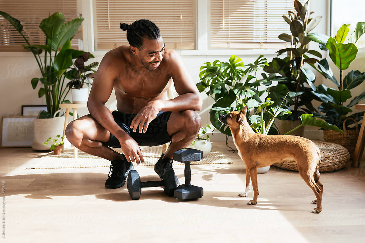 Happy ethnic sportsman looking at dog during break in training