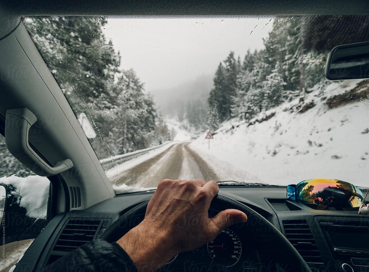 Anonymous man traveling and holding hands on the wheel driving on the snowy road mountain