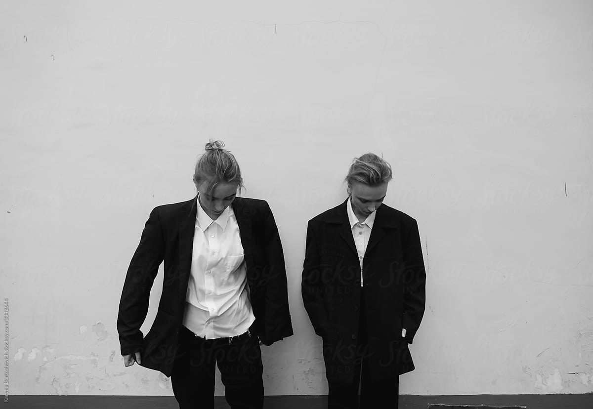 black and white portrait of two sisters against a white wall dressed in strict dark suits with gathered hair