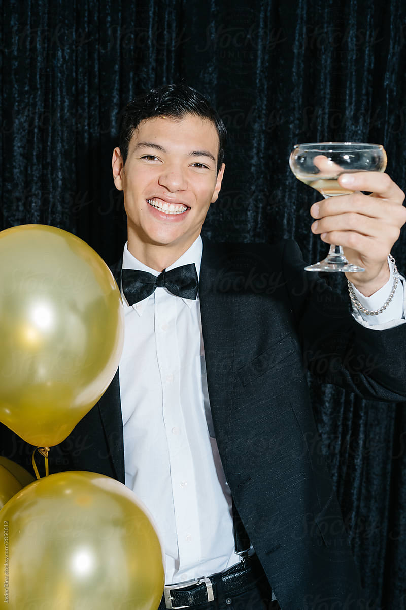 Handsome young man with golden balloon cheering with wine